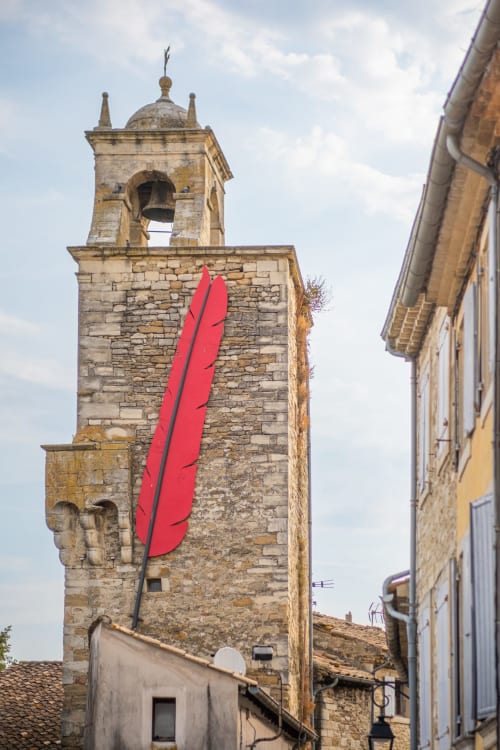 Torre d'église médiévale en pierre à Grignan avec installation artistique de plume rouge audacieuse, La vie de château à proximité