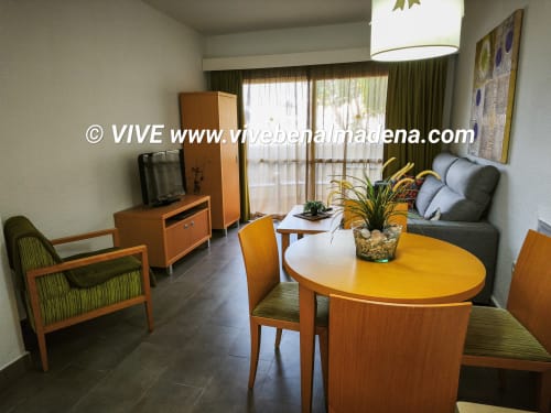 Sala de estar con vistas al jardín, mesa de comedor de madera, sofá, televisión y acceso a terraza en VIVE Benalmádena
