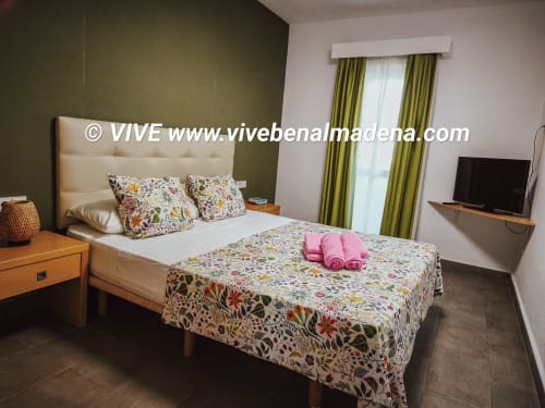 Bedroom at VIVE Benalmádena with cream headboard, floral bedding, garden view, olive walls, and flat-screen TV