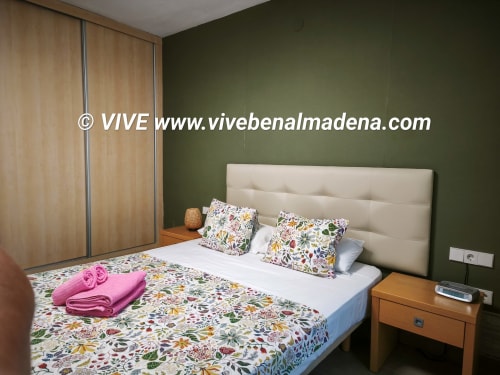 Benal Beach apartment bedroom with green walls, beige headboard, floral bedding, wooden wardrobe and nightstand in