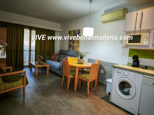 Modern apartment living room with kitchen, dining area, sofa, and garden views at VIVE Benalmádena