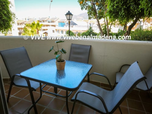 Terrace with blue table and chairs overlooking Benalmádena gardens and Mediterranean architecture at VIVE Benal Beach