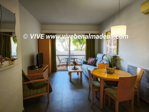Modern living room with dining area in garden-view apartment at VIVE Benalmádena, featuring wooden furniture and balcony