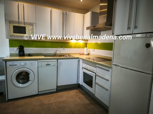 Modern kitchen with white cabinets, green tile backsplash, stainless steel appliances, washing machine, and wood countertops
