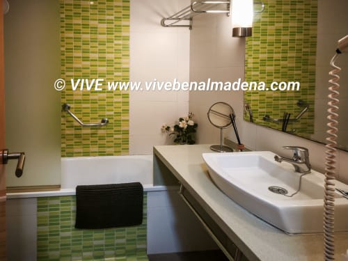 Modern bathroom with dual white sinks, green tiled walls, mirrors, and bathroom amenities at VIVE Benalmádena apartment