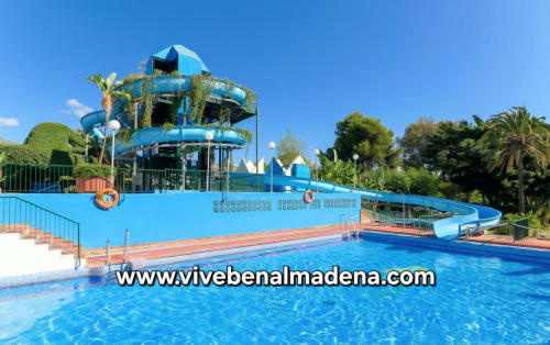 Blue water park with twisting slides at VIVE Benalmádena resort in Spain, surrounded by lush gardens and palm trees under