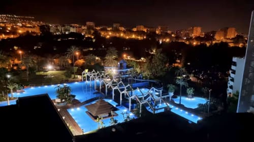 Illuminated blue swimming pools with lounge chairs at VIVE Benalmádena resort at night, Benalmádena Spain