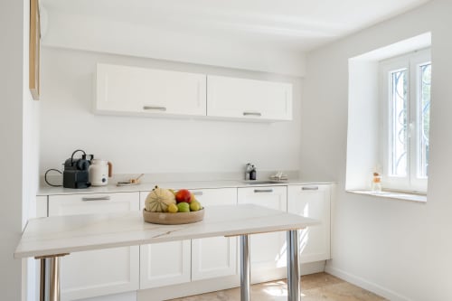 Modern white kitchen with island counter, fresh fruit bowl, and appliances in M Résidences villa near Cannes
