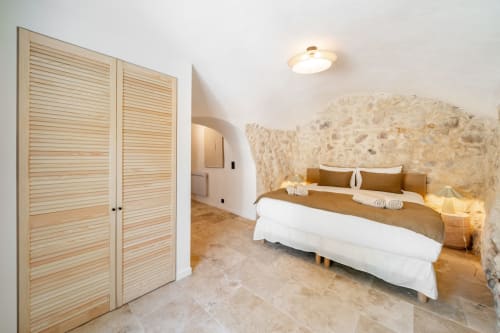 Bedroom with stone accent wall, wooden louvered doors, and terracotta bedding at Villa M de Mas near Cannes, France