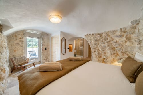 Spacious bedroom with rustic stone walls, arched ceiling, beamed flooring, and modern amenities in M Résidences villa in