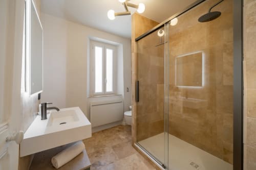 Modern bathroom in Villa M de Mas with rainfall showerhead, floating sink, and warm travertine tiling, Grasse, FR