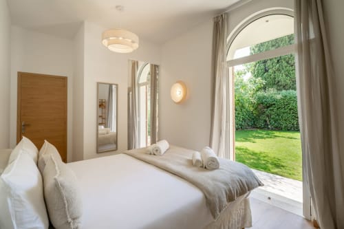 Bright bedroom in M Résidences villa near Cannes with white bedding, garden views through arched doors, and modern amenities