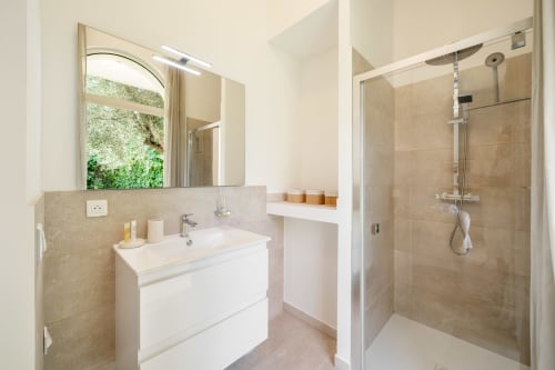 Modern bathroom in Villa M de Mas-Piscine, Grasse with white vanity, arched window, and walk-in shower with glass enclosure