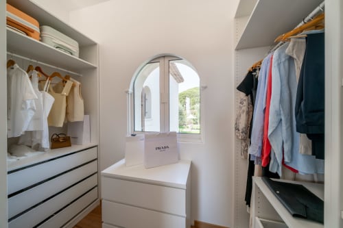 Luxury villa walk-in closet with white cabinetry, wooden hangers, clothing racks, and arched window in Grasse