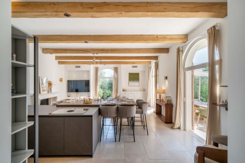 Modern villa kitchen and dining area with exposed beams, island seating, and terrace doors opening to garden views in Grasse