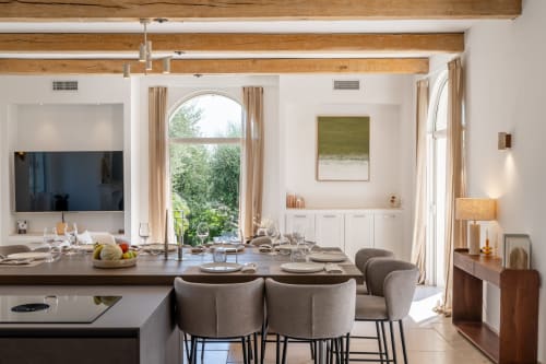 Modern villa dining room with exposed beams, set table, TV, and garden views in Grasse