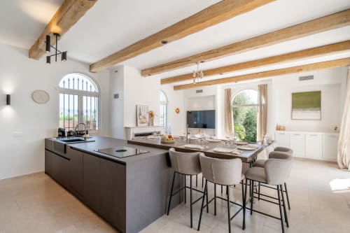 Modern open-plan kitchen and dining area in Grasse villa with exposed beams, island seating, and garden views