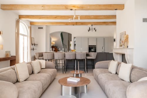 Modern open-plan living area with beige sofas, dining chairs, and wood beams in Villa M, Grasse
