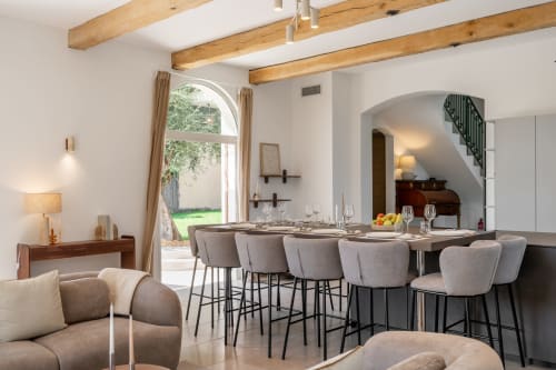 Modern dining area with gray upholstered chairs, wooden beams, and arched doorway in Villa M de Mas, Grasse