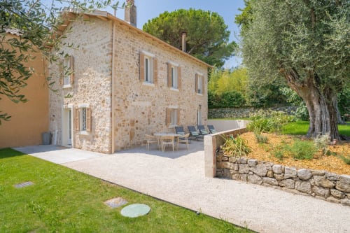 Stone villa in Grasse with terrace, lounge chairs, olive tree, and manicured gardens under sunny sky