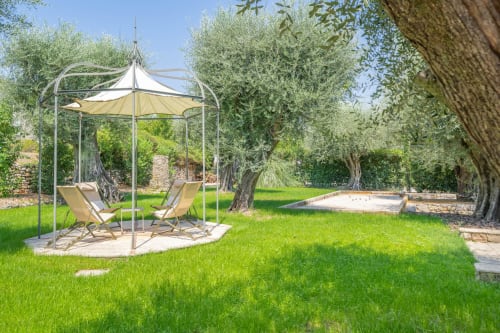 Luxury villa garden with pergola seating area, loungers, and sand pit surrounded by olive trees in Grasse, France