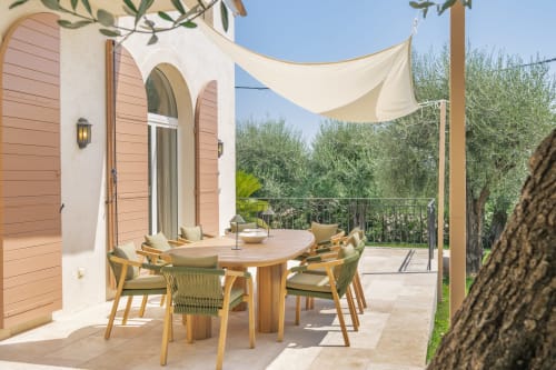 Sunny terrace with wooden dining table, green chairs, cream shade sails, and olive trees at M Résidences villa in Grasse