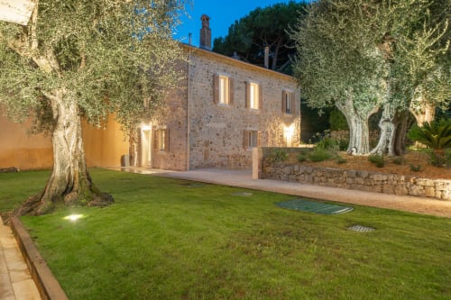 Stone villa at dusk with manicured lawn, ancient olive trees, and illuminated windows in Grasse, France
