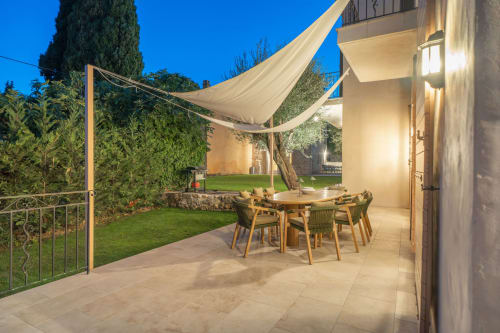 Evening patio at Villa M de Mas with dining table, cream shade sails, lit terrace, lush garden and olive tree in Grasse