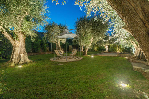 Elegant garden at Villa M in Grasse with ancient olive trees, gazebo, lounge chairs, and manicured lawn at dusk