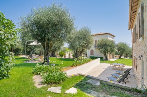 Tuscan villa courtyard with olive trees, manicured lawn, lounge chairs, and stone buildings at M Résidences et Hôtels