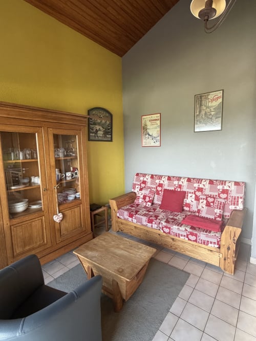 Salon cosy de La Devinière à Gérardmer avec mobilier en bois, canapé rouge à motifs et vue sur le lac