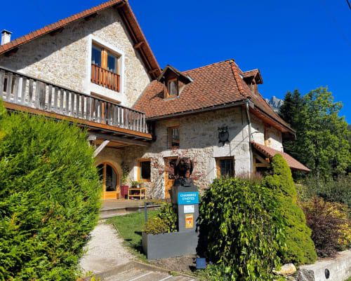 Cottage Le ValOmbré en Saint-Pierre-de-Chartreuse con fachada de piedra, balcón y vistas a las montañas bajo un cielo azul despejado