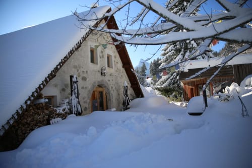 Cabaña cubierta de nieve en Le ValOmbré en Saint-Pierre-de-Chartreuse con muros de piedra, puerta de madera y vistas del bosque alpino