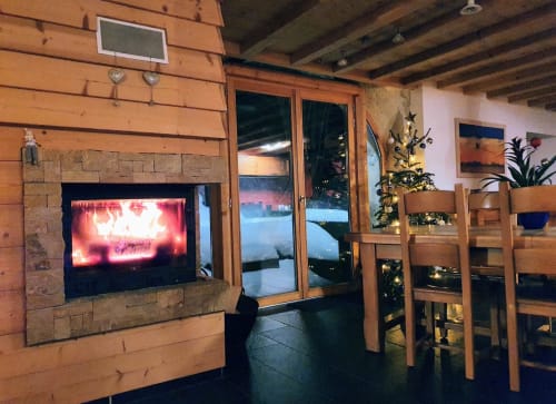Acogedor salón del cottage Le ValOmbré con chimenea, muebles de madera y vistas a las montañas a través de las puertas de vidrio
