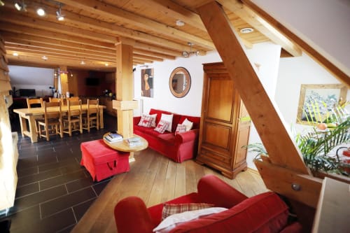 Sala de estar de la cabaña Le Grand ValOmbre con sofá rojo, vigas de madera y vistas a las montañas en Saint-Pierre-de-Chartreuse