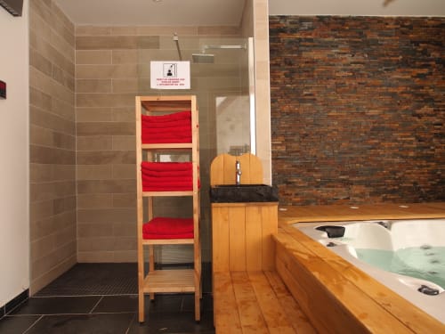 Baño moderno con toallero de madera, revestimiento de bañera en madera, área de ducha y pared de ladrillos expuestos en la casa rural Le Grand ValOmbre