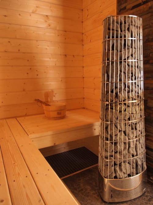 Interior de la sauna en la cabaña Le ValOmbré en Saint-Pierre-de-Chartreuse con paredes de madera y estufa de barril de piedra caliente