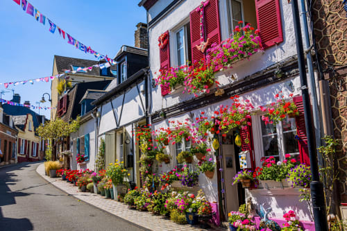 Charmante rue du village au château de Mons Boubert avec cottages aux volets roses et corbeilles de fleurs colorées