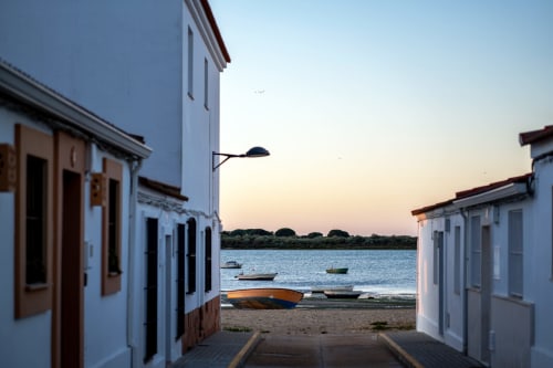 Callejón junto a la playa en Hotel Plaza Chica en Cartaya con edificios blancos, barcas y vista al agua al atardecer