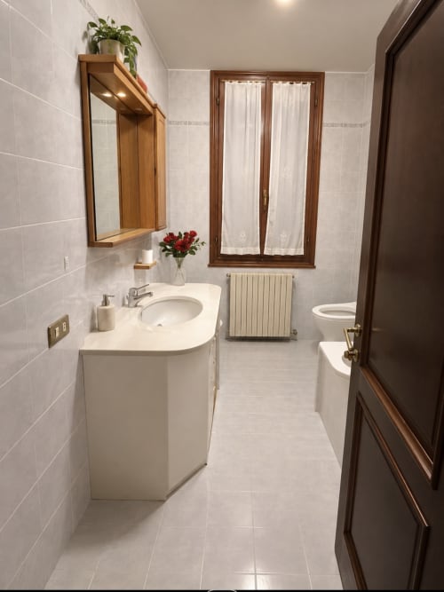Modern bathroom in Venice luxury apartment with white tile walls, wooden mirror, red flowers, and heated radiator