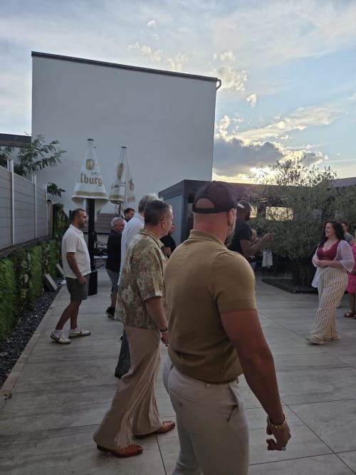 Guests mingling on terrace at Hôtel-Restaurant le S'Y in Seingbouse with beer umbrellas and sunset sky