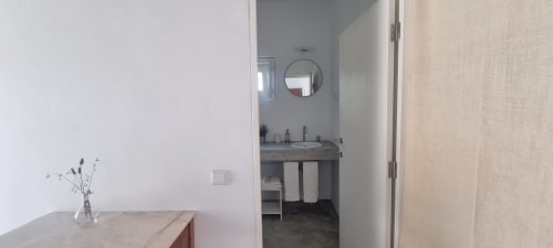 Entrada moderna do banheiro da Monte Falperras BnB em Mourão com pia de penteadeira, espelho redondo e acesso ao quarto com vista para o jardim