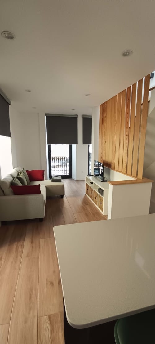 Modern apartment living area at Pés Verdes Hostel with beige sofa, wooden flooring, dining table, and wooden partition wall