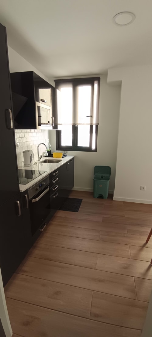 Modern black kitchen with white subway tile backsplash, sink, stove, and large window in Pés Verdes Hostel apartment, Ponta