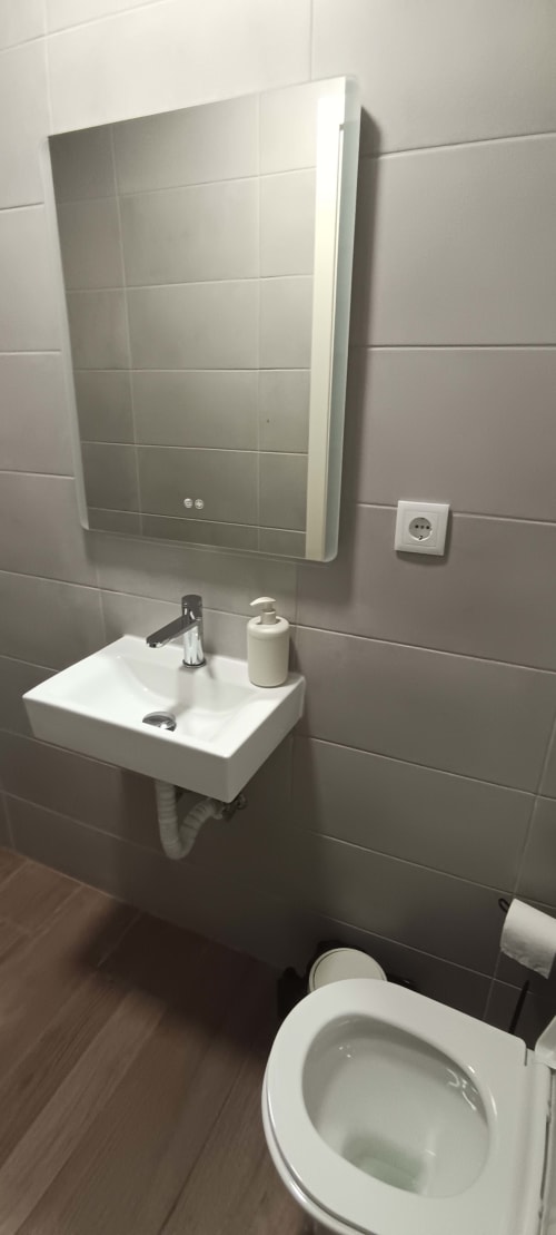 Modern bathroom at Pés Verdes Hostel with illuminated mirror cabinet, white sink, and toilet in Ponta Delgada