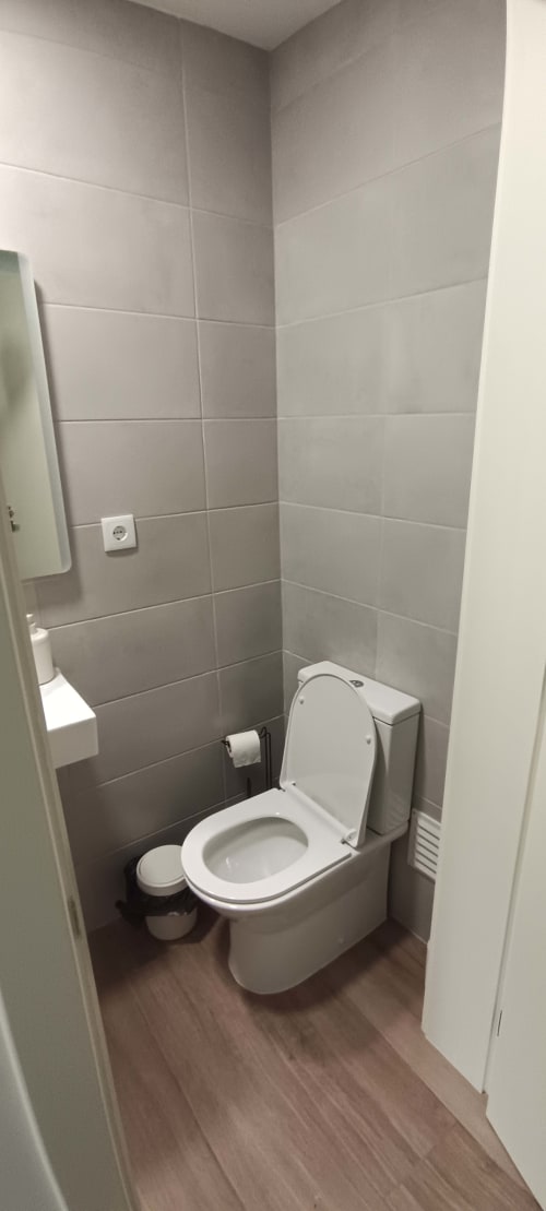 Compact bathroom in Pés Verdes Hostel apartment with white toilet, tiled walls, towel rack, and wooden floor in Ponta