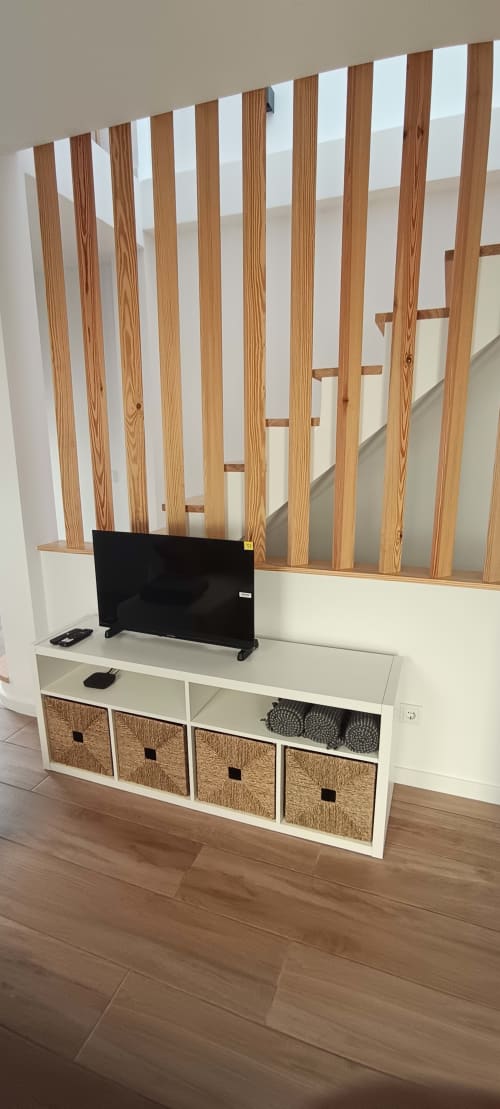 Modern TV stand with wooden slat backdrop at Pés Verdes Hostel apartment in Ponta Delgada, featuring white storage with woven