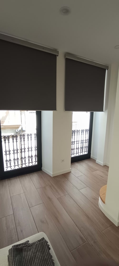 Modern apartment living area at Pés Verdes Hostel with wooden floors, dual glass doors opening to city balconies, and black