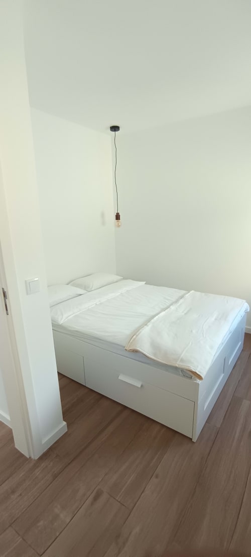 Minimalist bedroom at Pés Verdes Hostel with white bed, wooden floors, and pendant light fixture in Ponta Delgada
