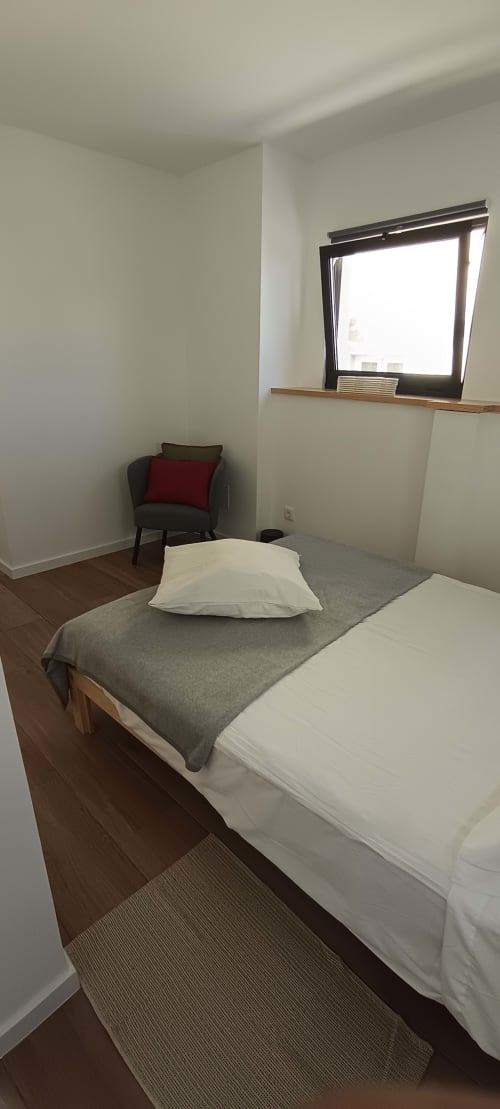 Bright bedroom at Pés Verdes Hostel in Ponta Delgada with bed, window, armchair, and wooden floors